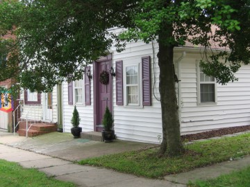 White house with maroon accents under green tree.