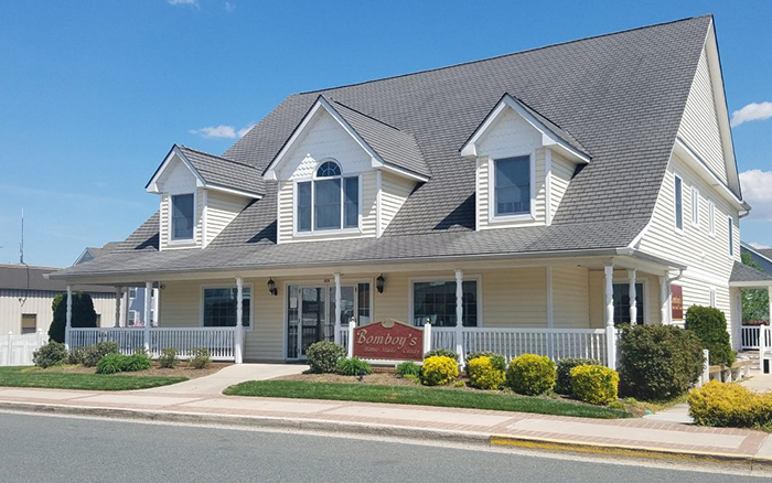 Front street view of large yellow homesyle building with dormer windows and wrap around porch.