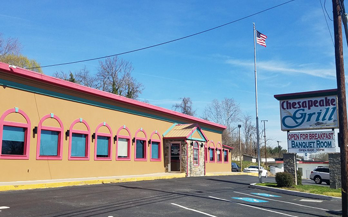 Parking lot view of long tan building with red trim and large sign outfront.