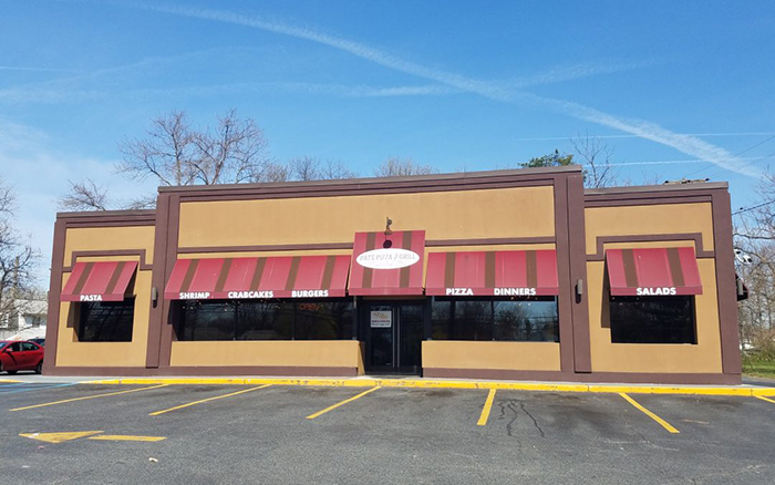 Parking lot view of tan pizza shop with red and brown stripped awnings.