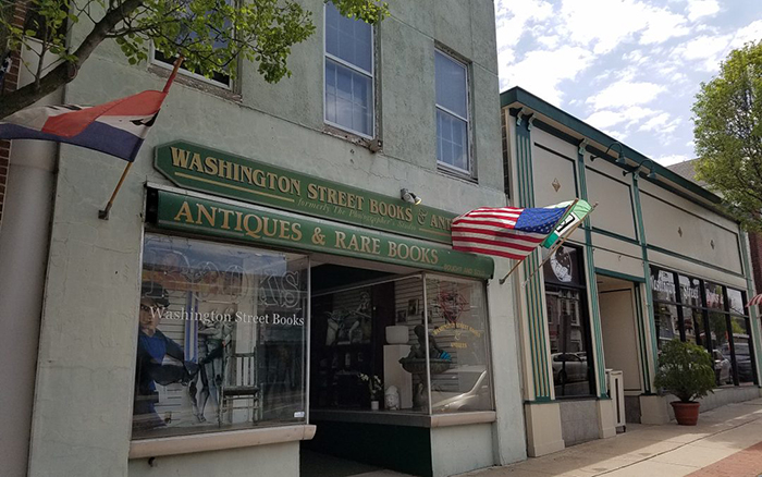 Two story paved city storefront with green banners and flags.