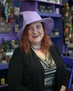 Witchy healing and learning space owner in Havre de Grace, Maryland, wearing a witch hat in front of spiritual nick knacks