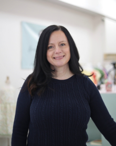 Children and baby boutique shop owner in Havre de Grace, Maryland, smiling in front of baby clothing