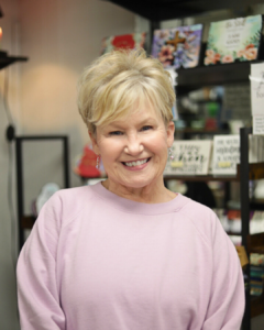 Boutique shop owner in Havre de Grace, Maryland, smiling in front of unique sign decorations