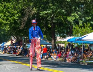 stilt walker walking down a packed street during a 4th of July parade dressed as Uncle Sam